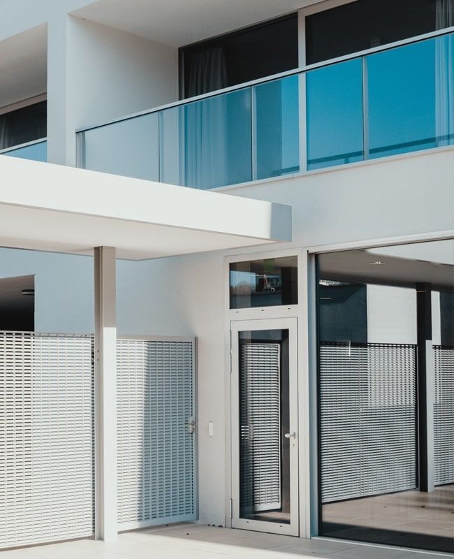 Edificio moderno blanco con balcón de cristal y portón de metal.