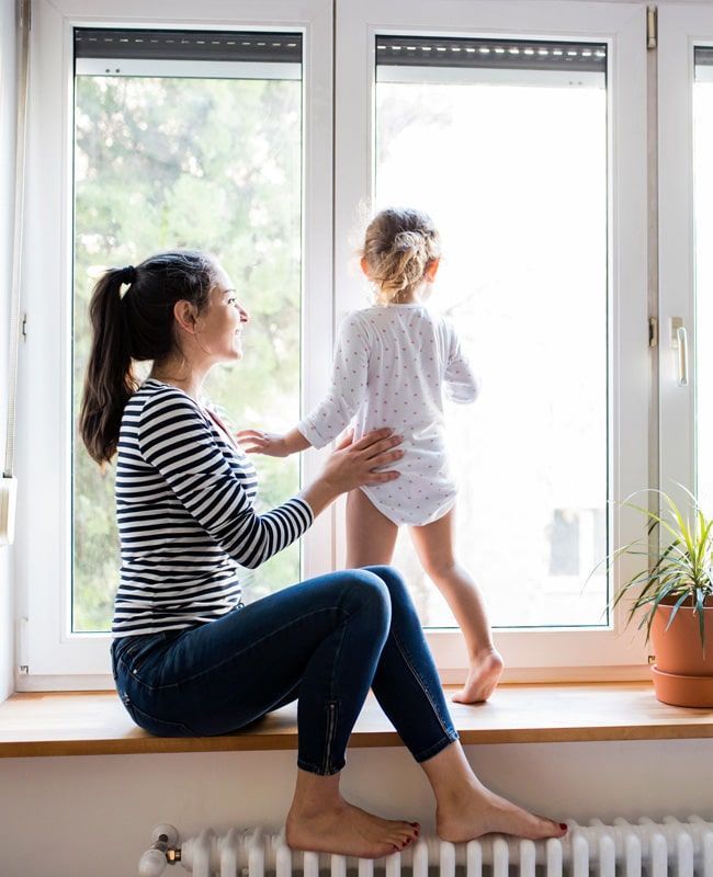 Una mujer se sienta en el alféizar de la ventana, toca la espalda de un niño pequeño y ambos miran por la ventana.