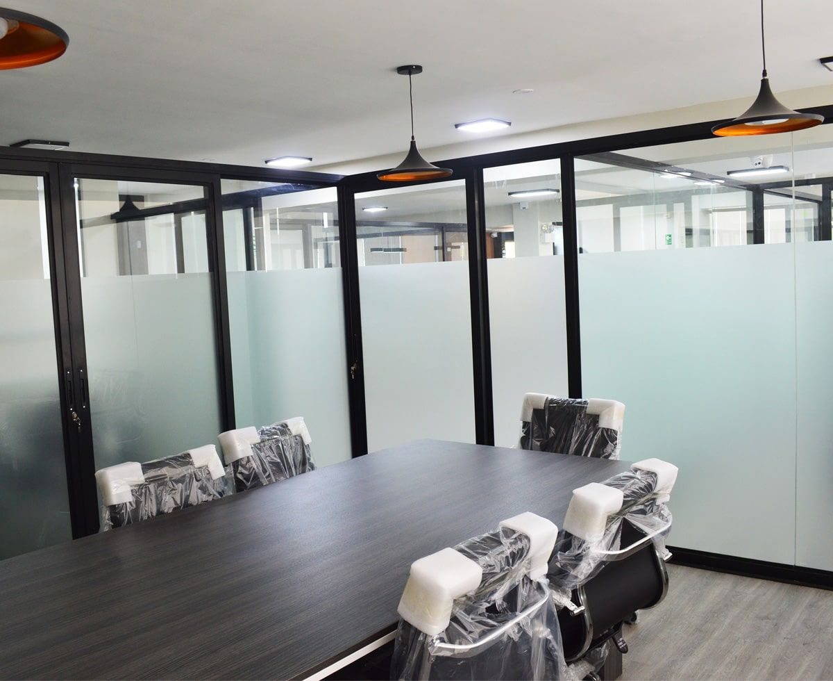 Sala de conferencias con mesa larga y sillas; paredes de vidrio esmerilado.