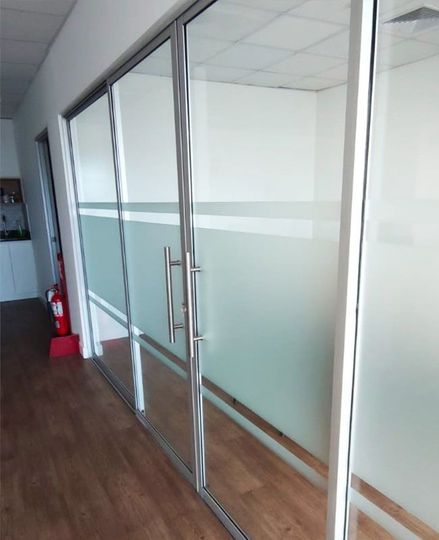 Puertas de oficina de vidrio con rayas esmeriladas. Suelo de madera reflectante y paredes blancas.
