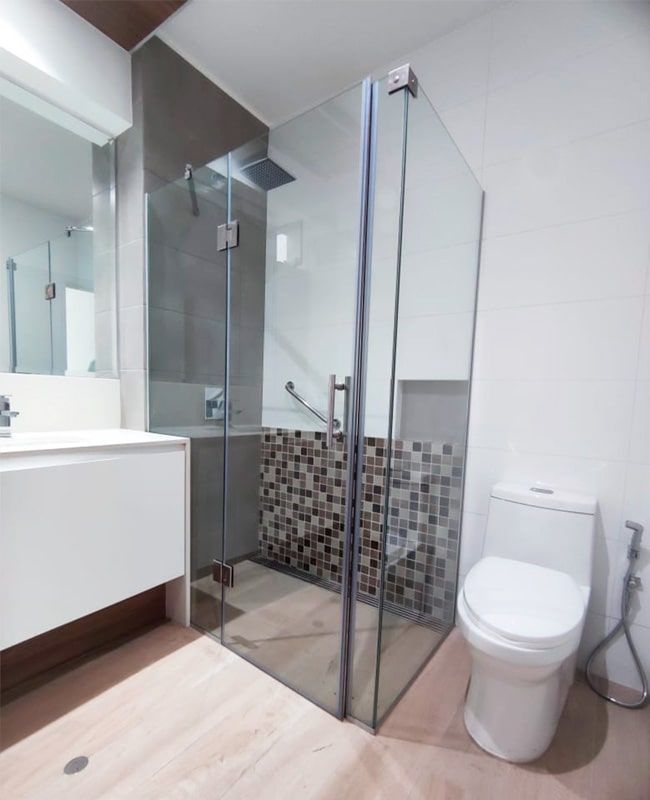 Baño moderno con ducha de cristal, inodoro y lavabo blanco. Colores neutros con detalles de mosaico.