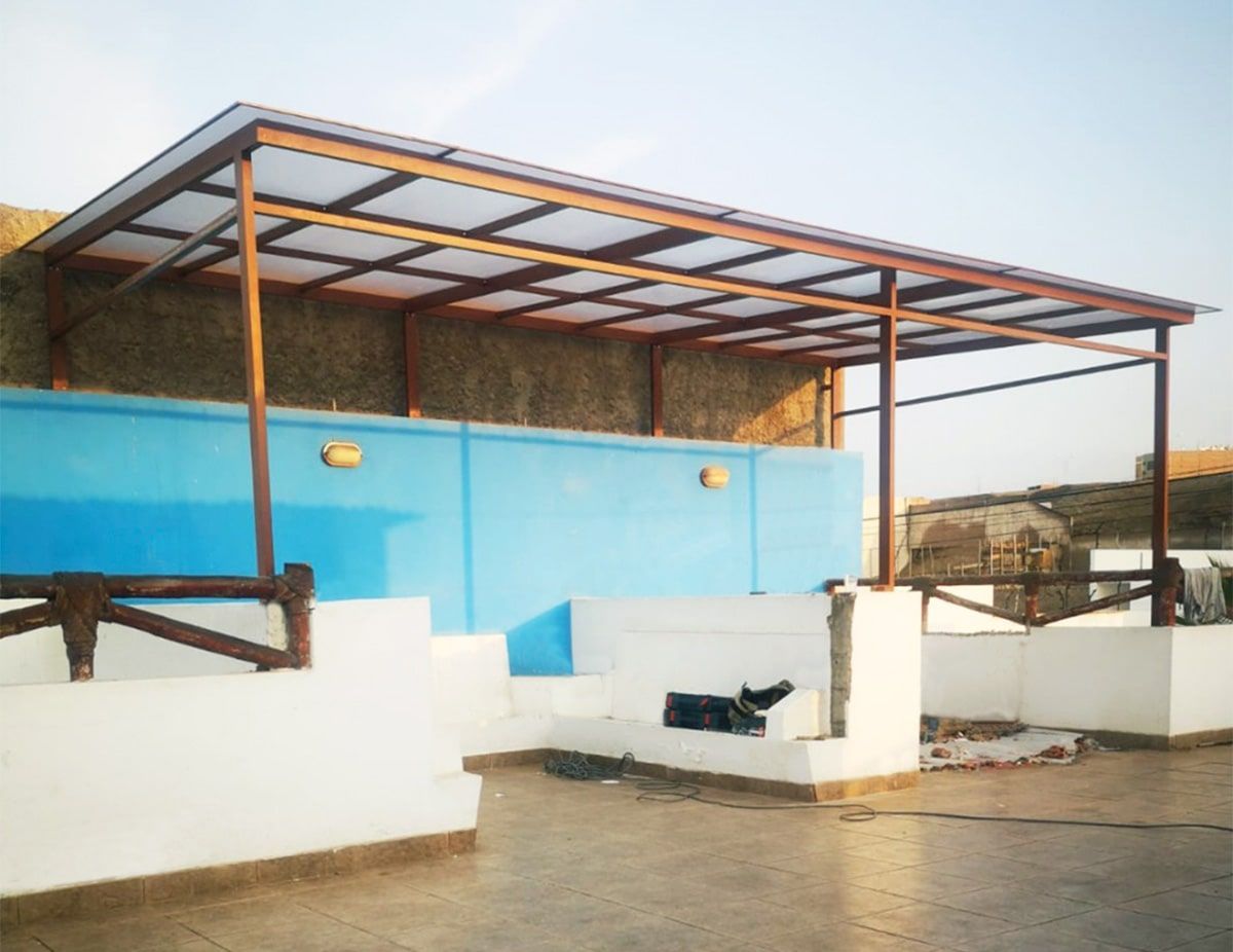 Un patio con techo de estructura metálica de color marrón, con vistas a una pared azul y estructuras blancas.
