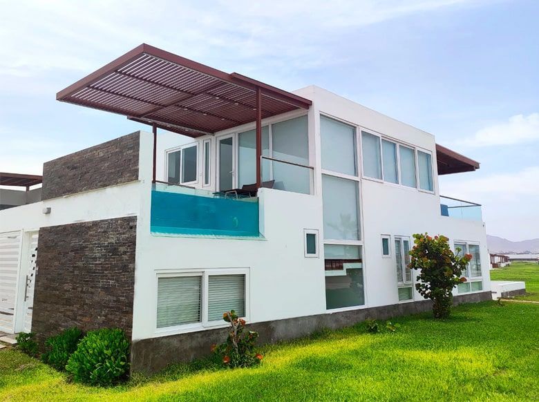 Casa blanca de dos pisos con techo plano, ventanas de vidrio y césped verde.