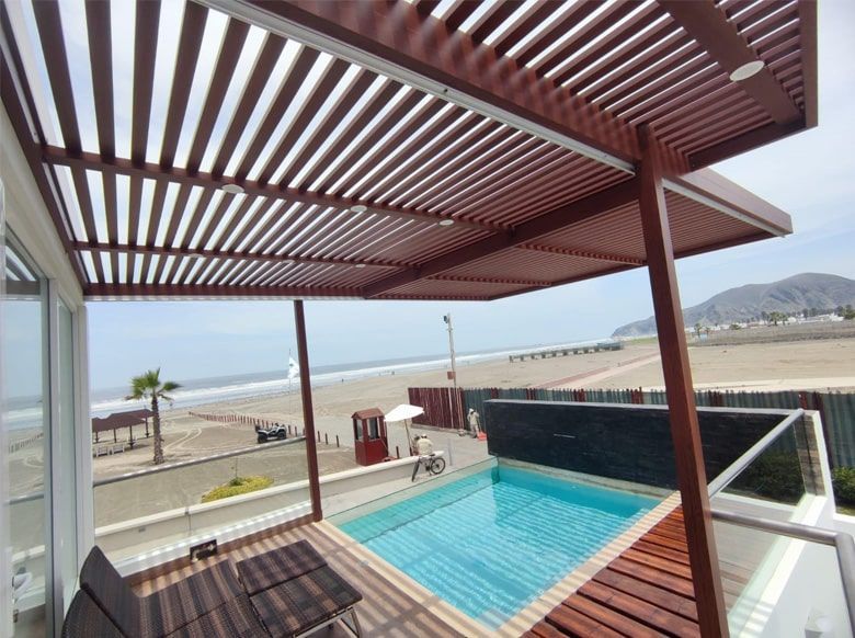 Piscina en patio con pérgola de madera, con vistas a la playa.