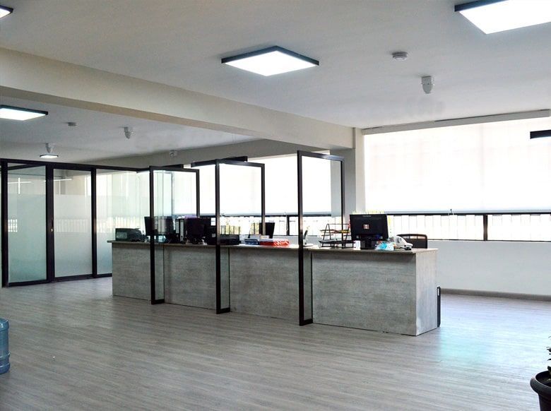 Espacio de oficina vacío con escritorios, divisores de vidrio, ventanas y luces de techo.