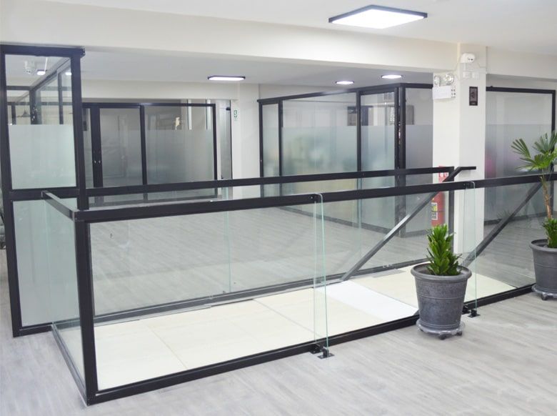 Interior de oficina moderno con paredes de vidrio, marco negro y barandilla.