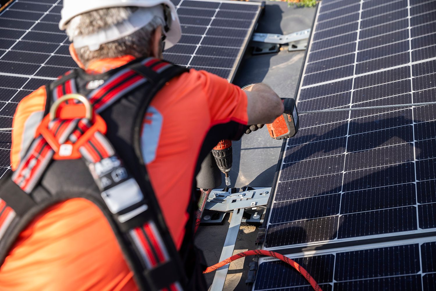 Arbeiter im Sicherheitsgurt installiert Solarmodule auf einem Dach.
