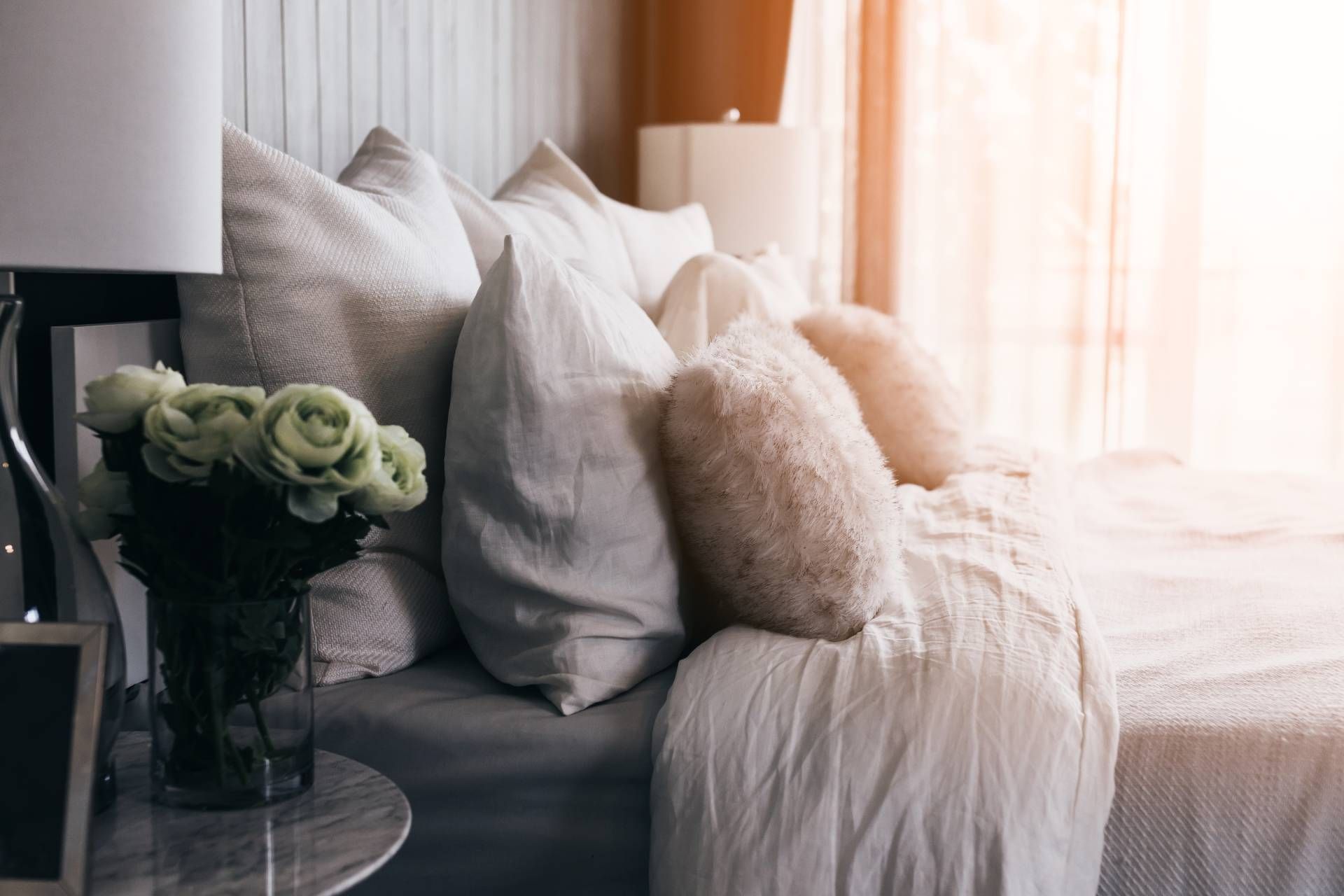 Cozy guest bedroom with layered window treatments, a comfortable bed, and flowers on the nightstand 