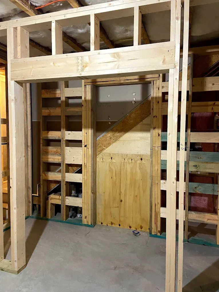 Unfinished wooden doorway framed by exposed studs in a basement or workshop area.