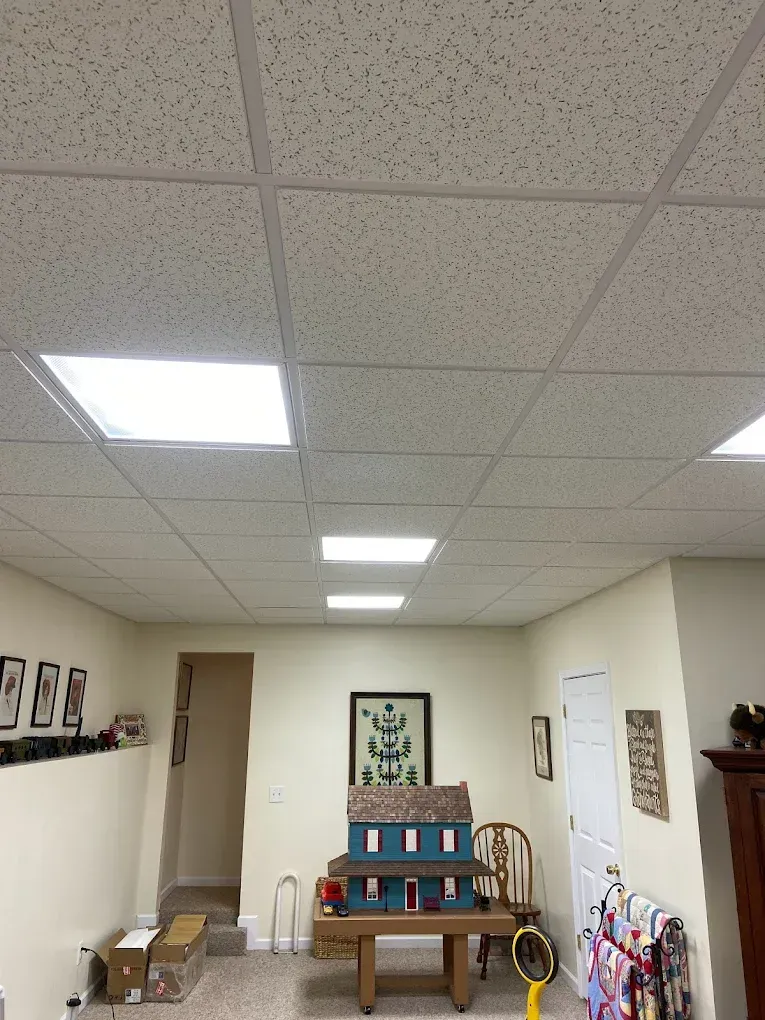 Small room with drop ceiling, wall art, bench, and stacked boxes near the back wall.