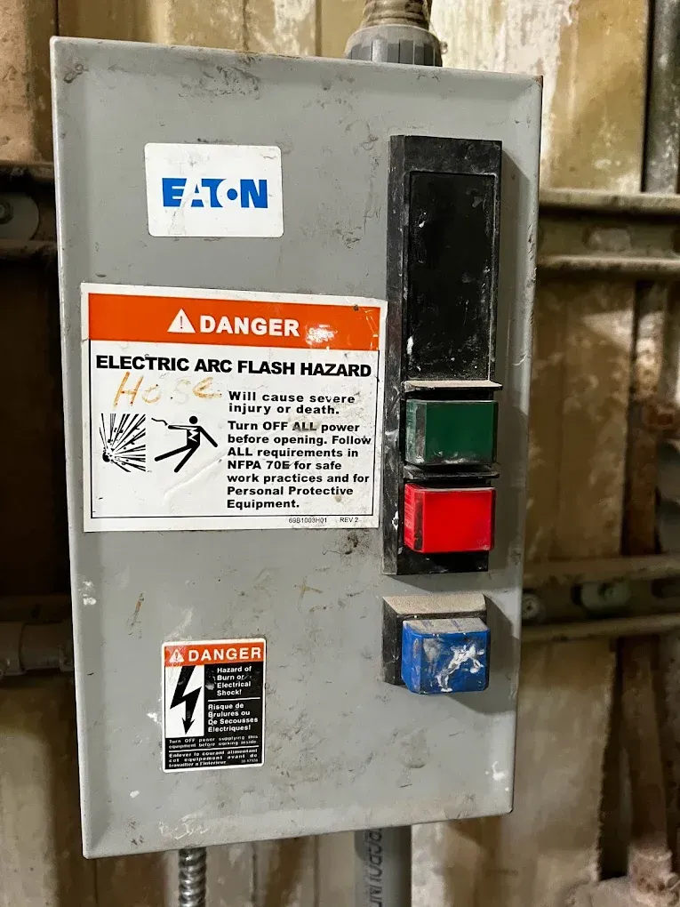 Gray Eaton electrical disconnect box with danger label and red/green buttons mounted on a wall