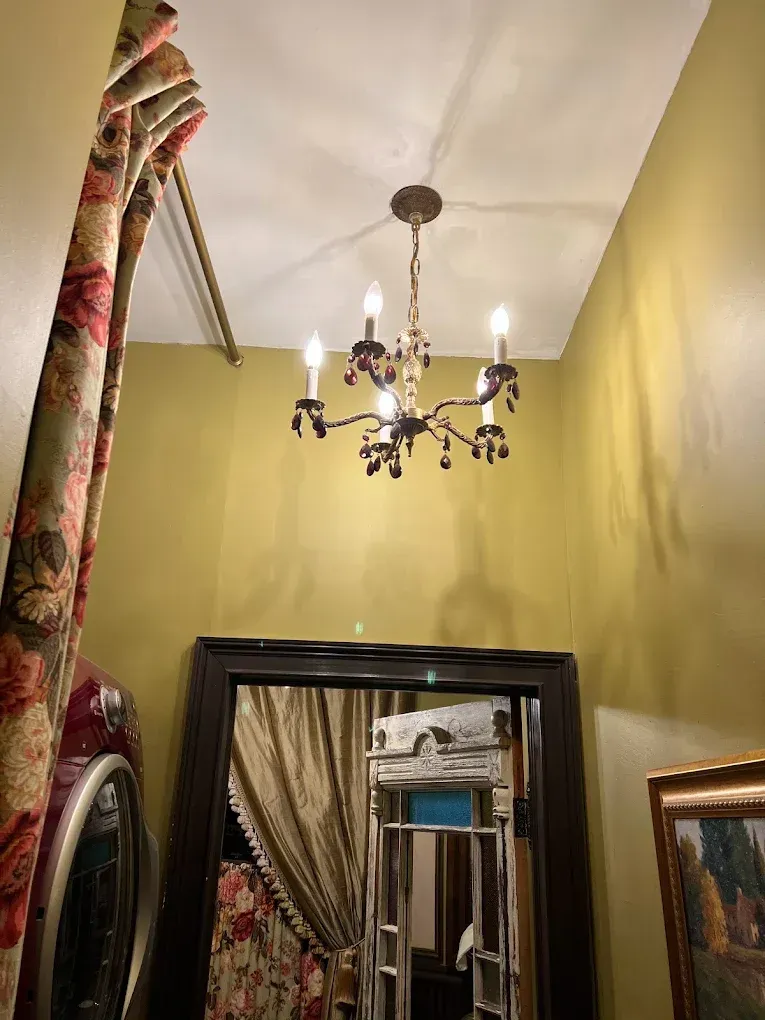 Hallway with pale yellow walls, ornate chandelier, and tall mirror reflecting a curtained doorway