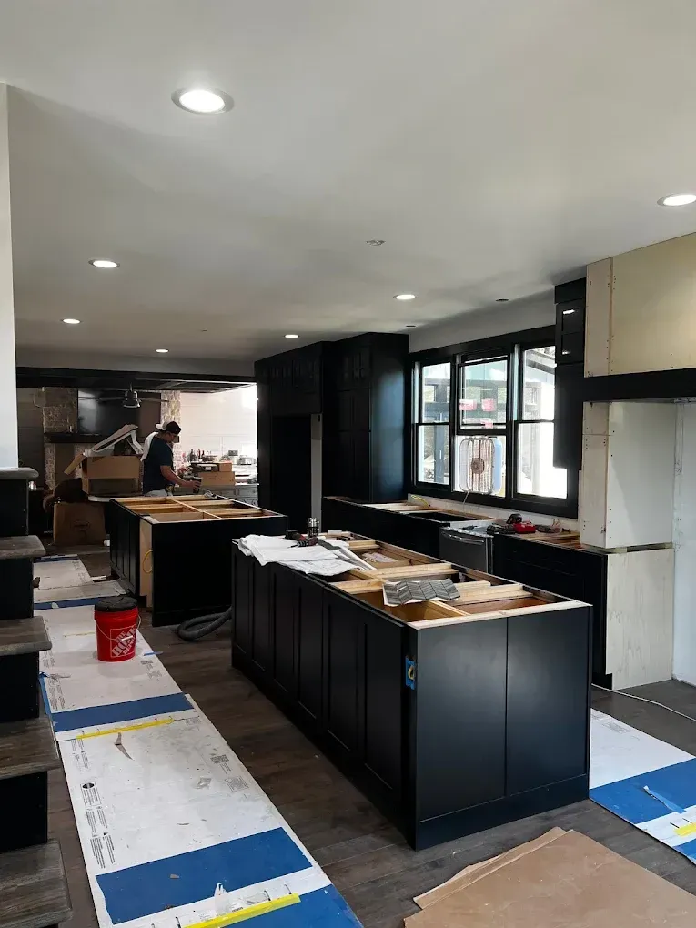 Kitchen renovation with cabinets and tools, workers in the background, and protective floor coverings