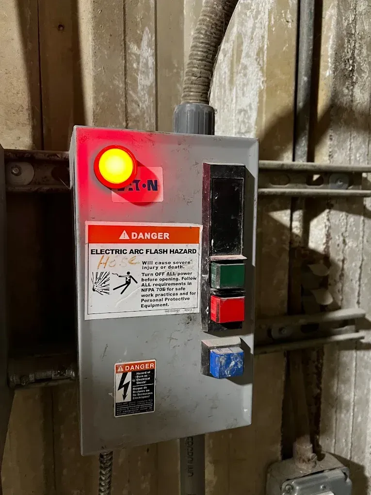 Red electrical control box with lit warning light and danger label on a wall
