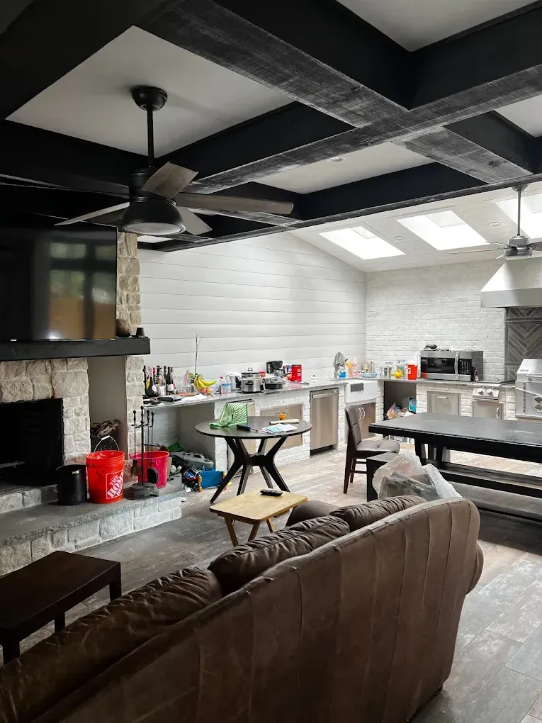Modern open-plan kitchen and living room with exposed ceiling beams, white walls, and a brown sofa in the foreground