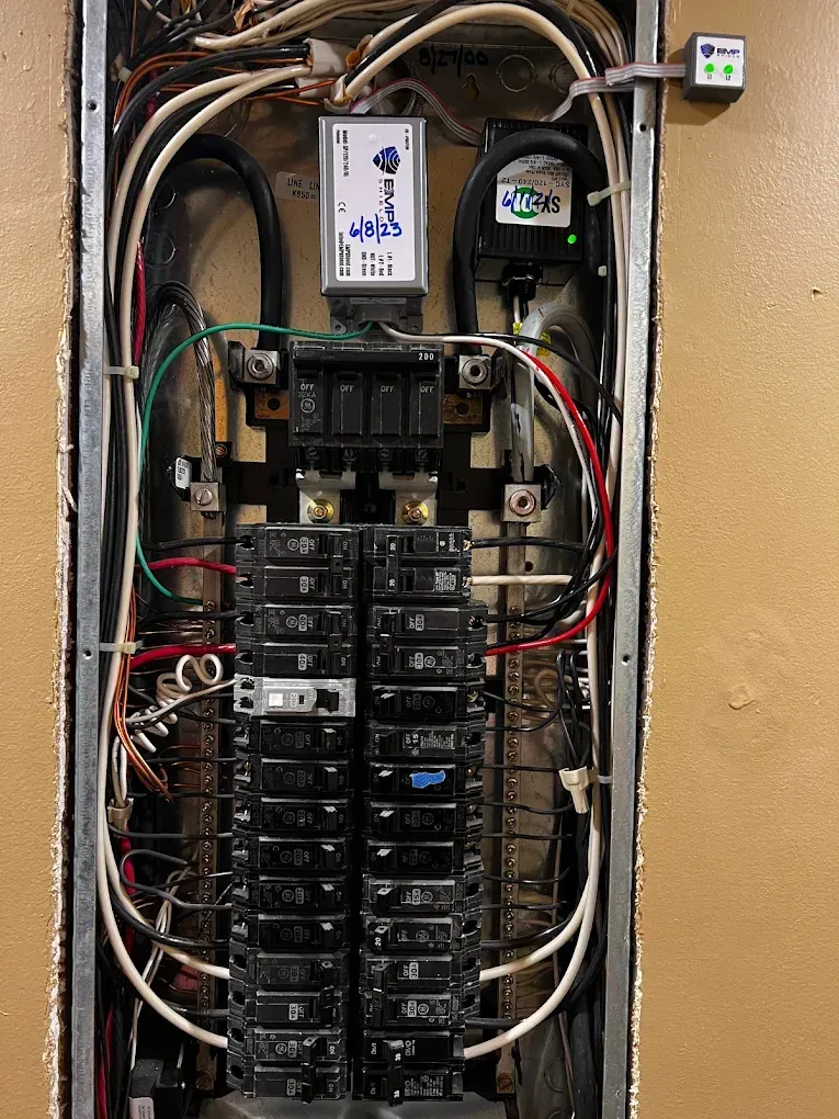 Open electrical breaker panel with tangled wires and meters mounted above it