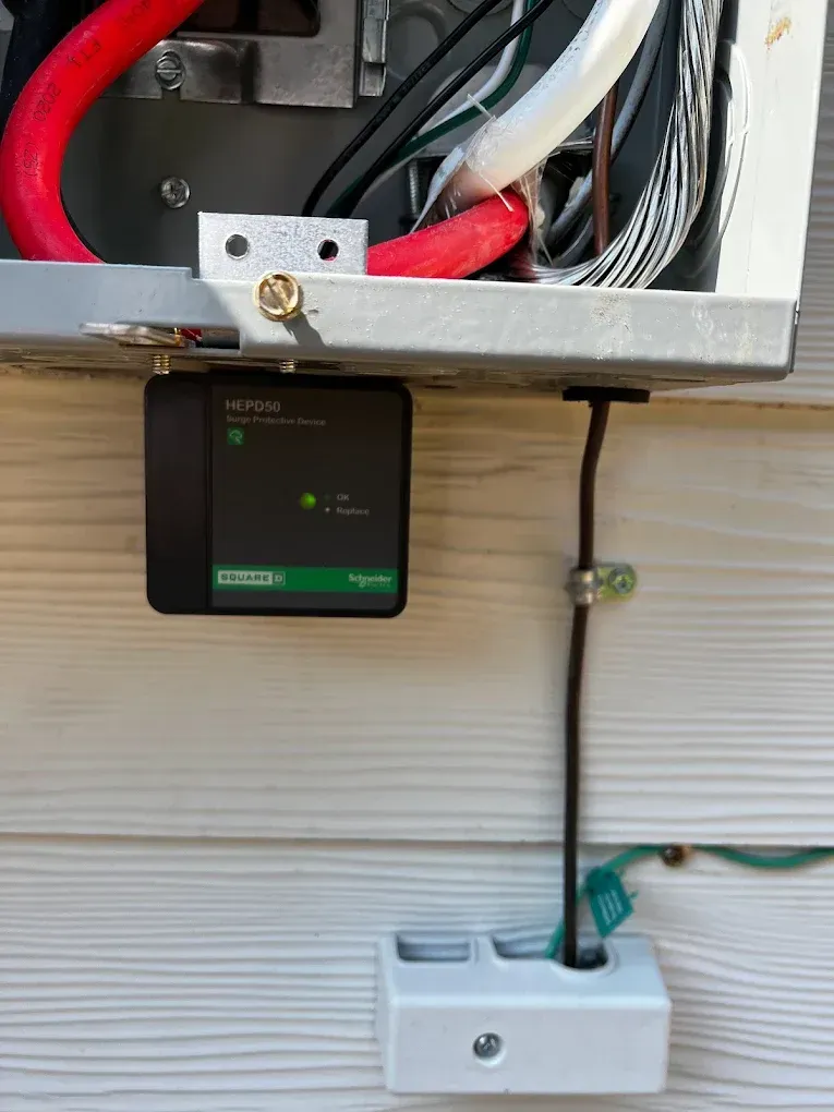 Black electrical control box mounted under an outdoor wall panel with exposed wiring and conduit