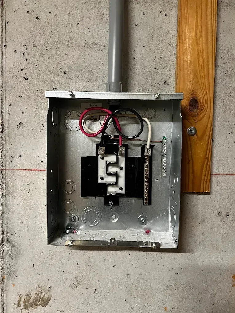 Open electrical junction box with exposed wiring on a concrete wall near a wooden stud.
