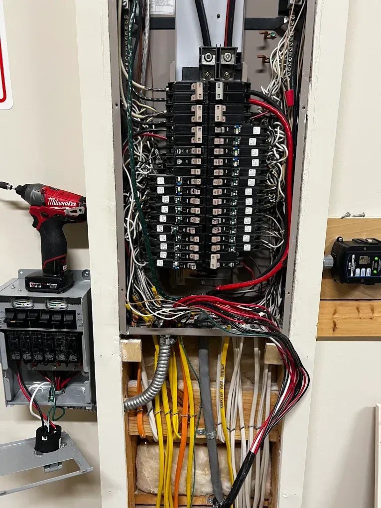 Electrical breaker panel with bundled wires and red/black power tools nearby