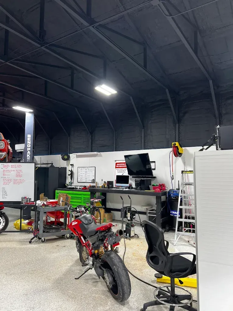 Motorcycles and tools in a workshop with a high dark ceiling and white storage cabinets