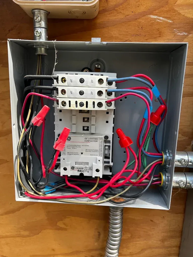 Open electrical breaker panel with exposed red and black wires and conduit in a metal box