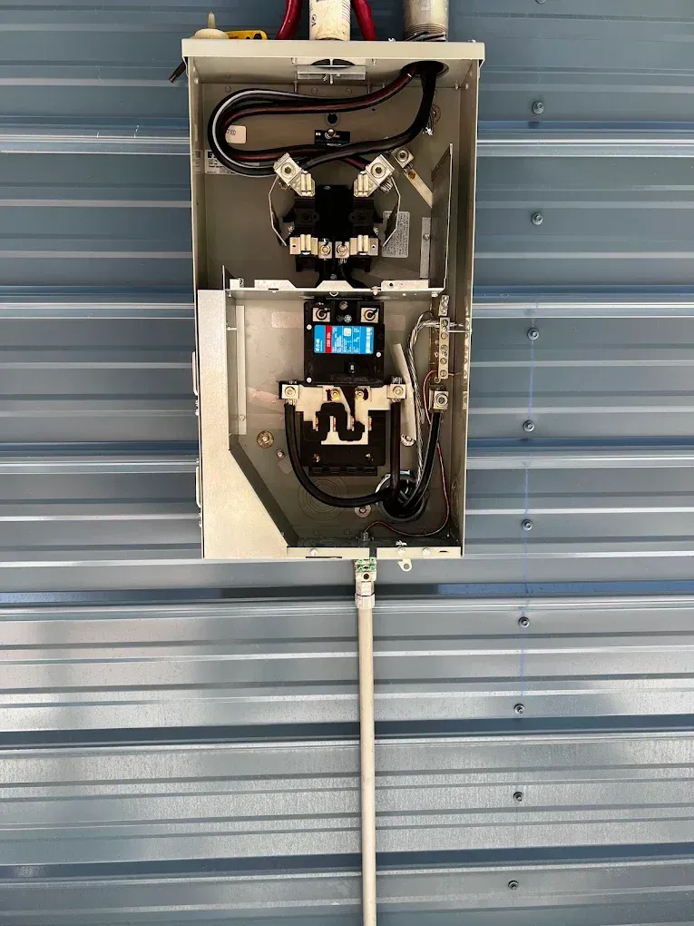 Open electrical control panel mounted on a blue metal wall, with wires and a display inside.
