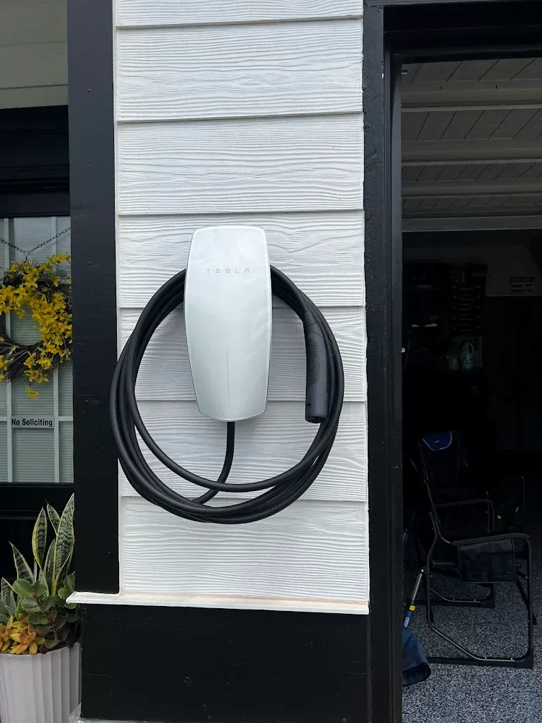 White wall-mounted EV charger with coiled black cable on a house exterior wall