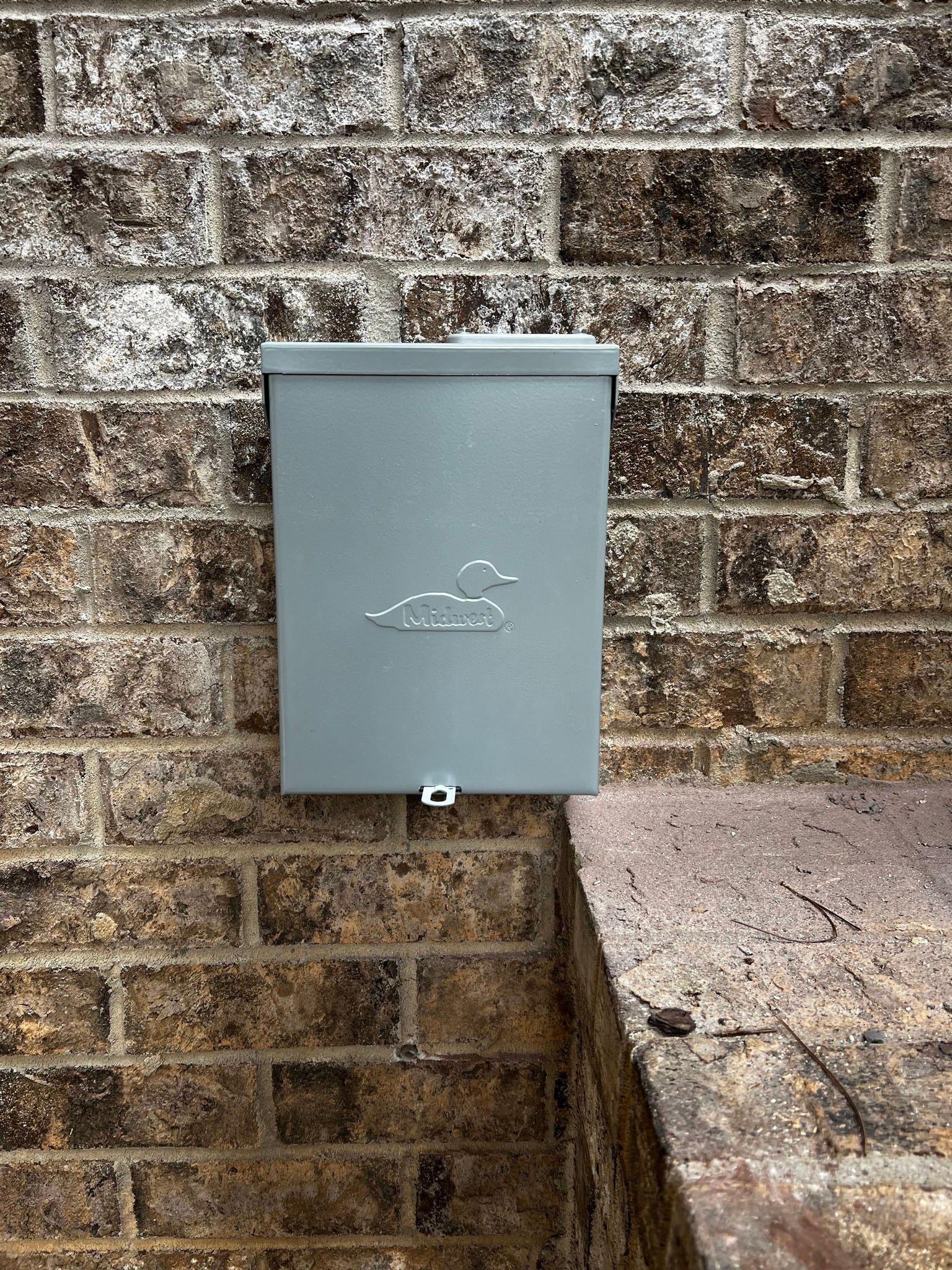 Gray wall-mounted utility box on a brick wall beside a concrete step.