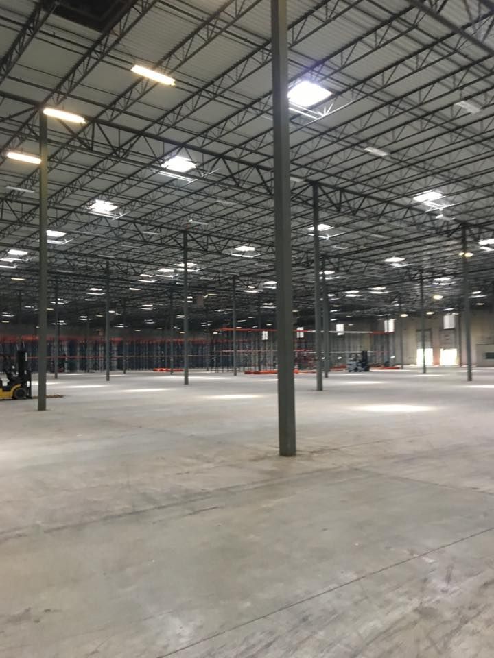 Empty industrial warehouse with concrete floor, metal support columns, and overhead lights