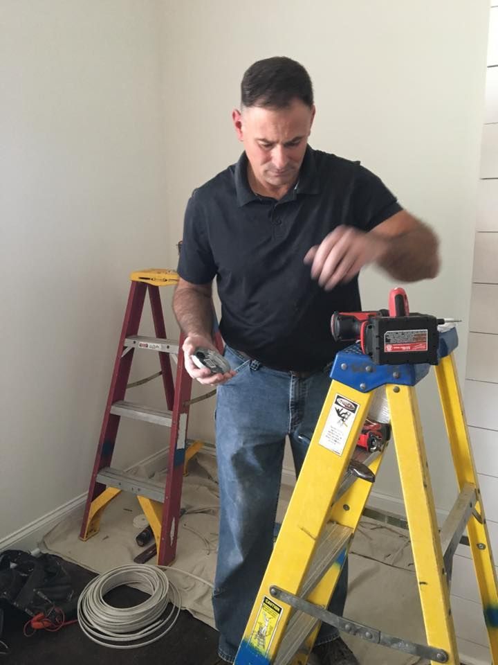 Electrician working on wiring near a yellow ladder in a room under renovation