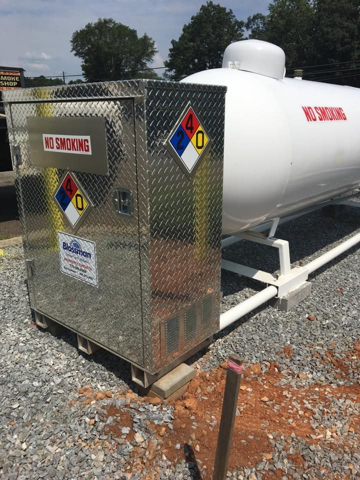 White hazardous-material tanker trailer with hazard placards and diamond-plate front end on gravel outdoors