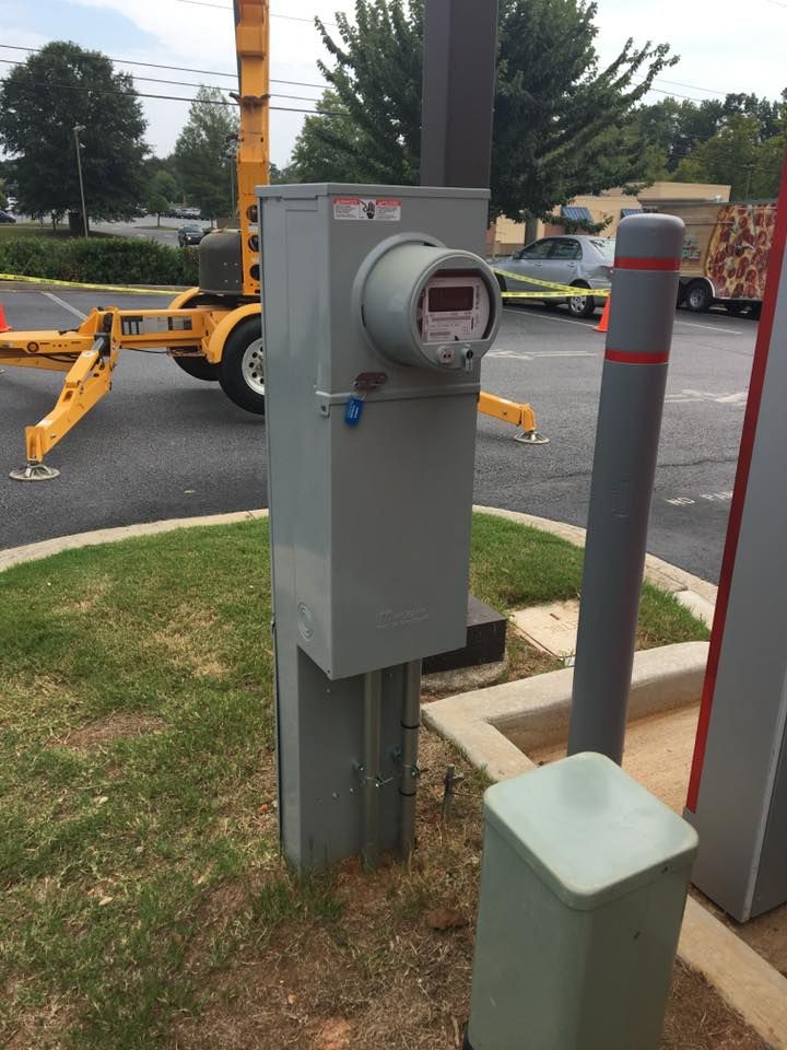 Parking lot utility meter pedestal beside a boom lift, with striped bollards and curb at right.