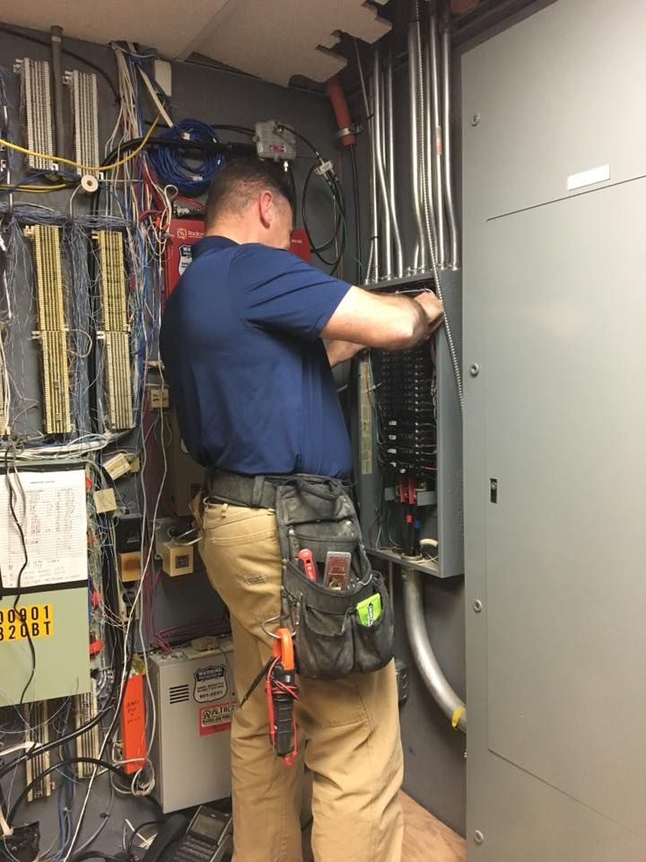 Technician working inside an electrical panel room with exposed wiring and gray cabinets