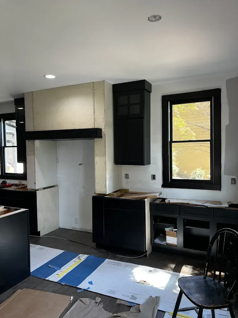 Kitchen under renovation with white cabinets, black trim, and sunlight through windows