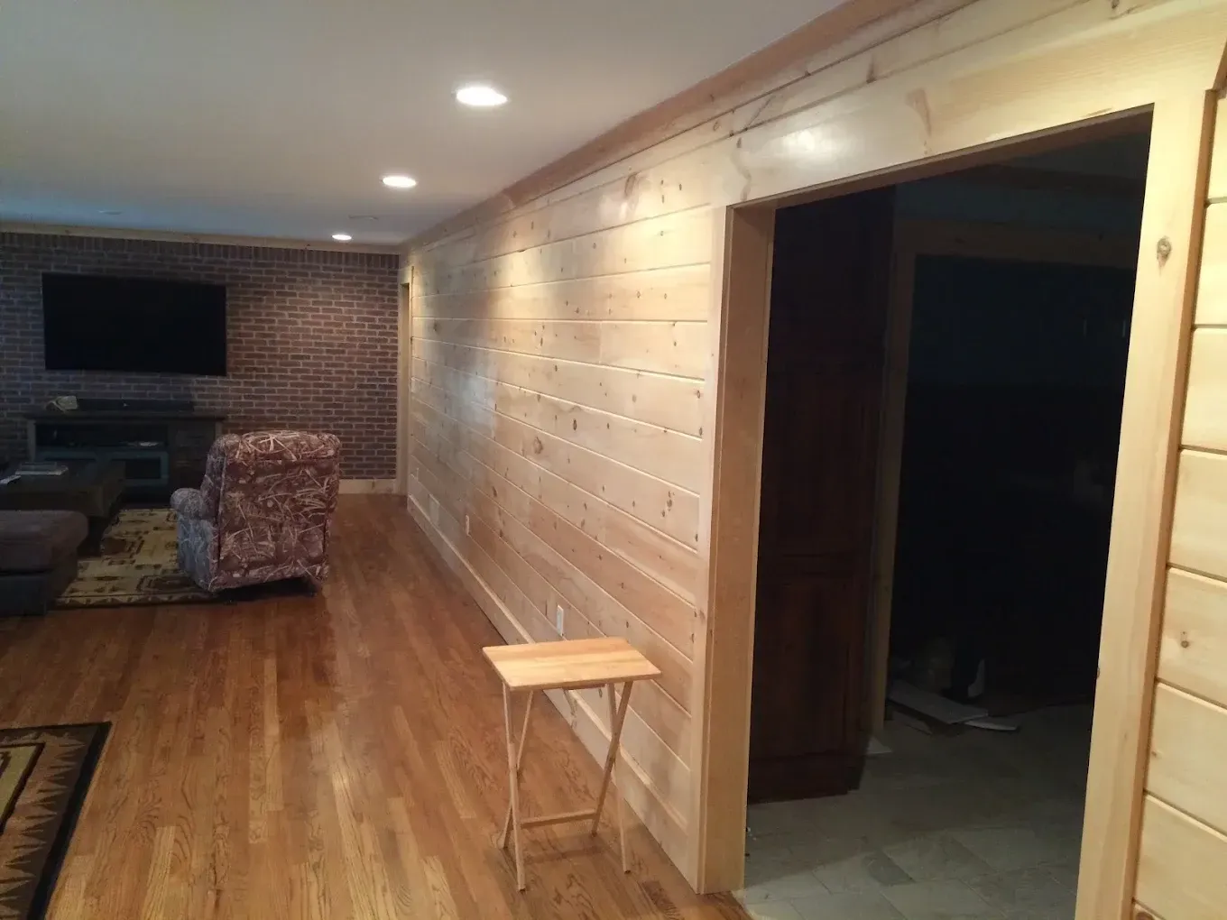 Wood-paneled hallway with wood floors, a small stool, and a dark room doorway on the right.