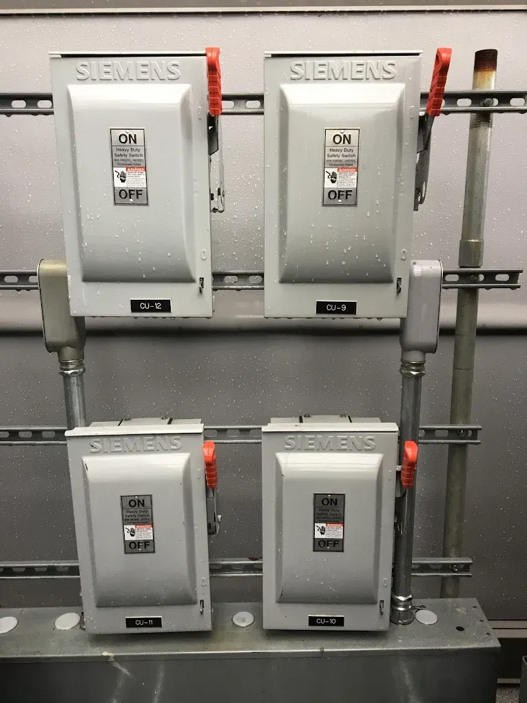 Four Siemens electrical breaker panels mounted on a gray industrial wall, with several switches in the OFF position