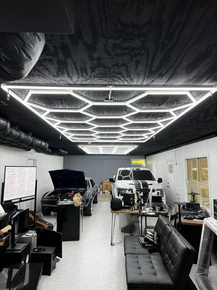 Large garage workspace with hexagonal LED ceiling lights, tools, shelves, couches, and vehicles under repair