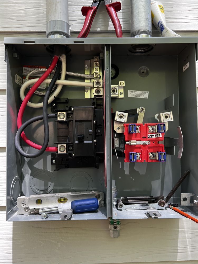 Open electrical breaker panel with wiring, black breaker, and red switch components outdoors