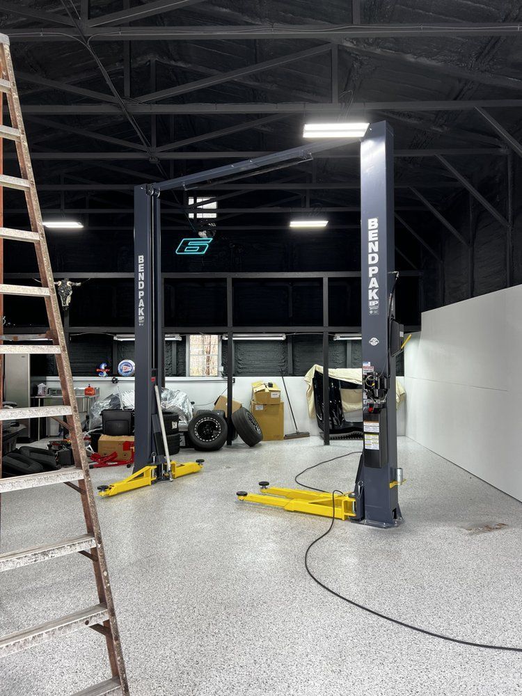 Auto repair shop with two vehicle lifts, ladder, and open bays under a high industrial ceiling