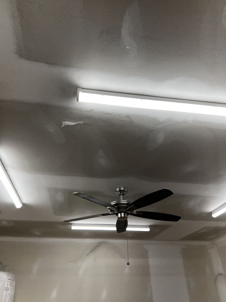 Ceiling with a black fan and fluorescent lights in a room with unfinished drywall