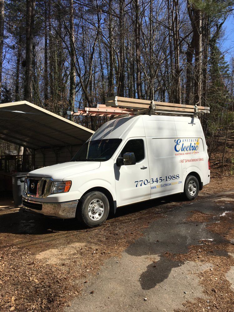 White work van with ladder racks parked outdoors beside an open dumpster in a wooded area.