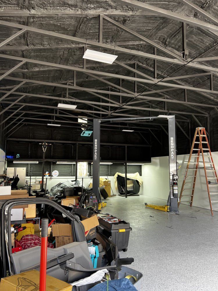 Indoor auto repair shop with vehicles, tools, lift posts, and a ladder under exposed roof beams