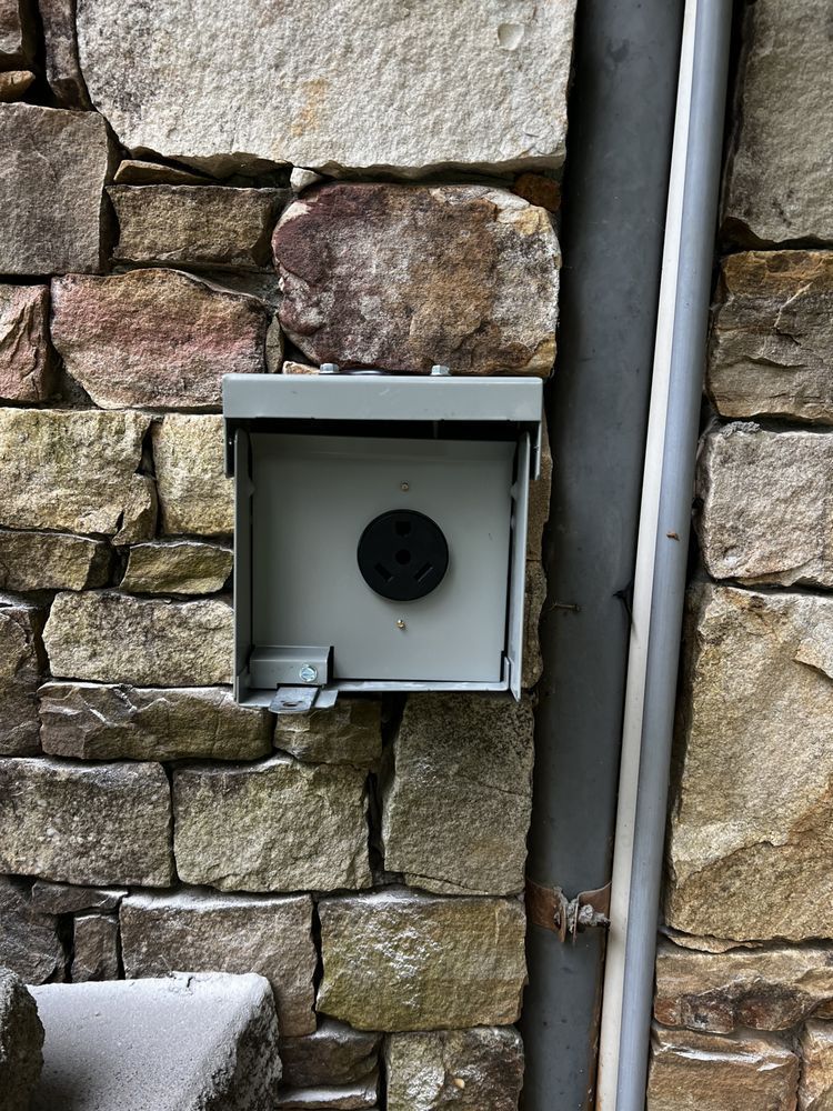 Open metal electrical box mounted on a stone wall with conduit beside it.