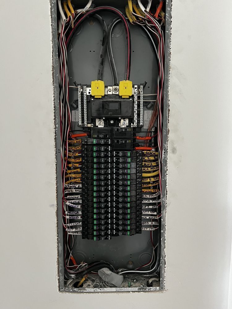 Open electrical breaker panel with colored wires and rows of circuit breakers in a wall recess