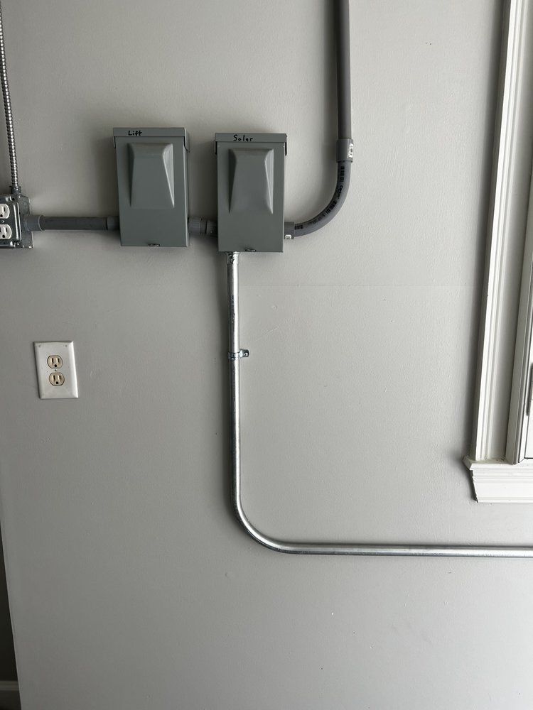 Two gray electrical boxes and conduit mounted on a light gray wall near an outlet.