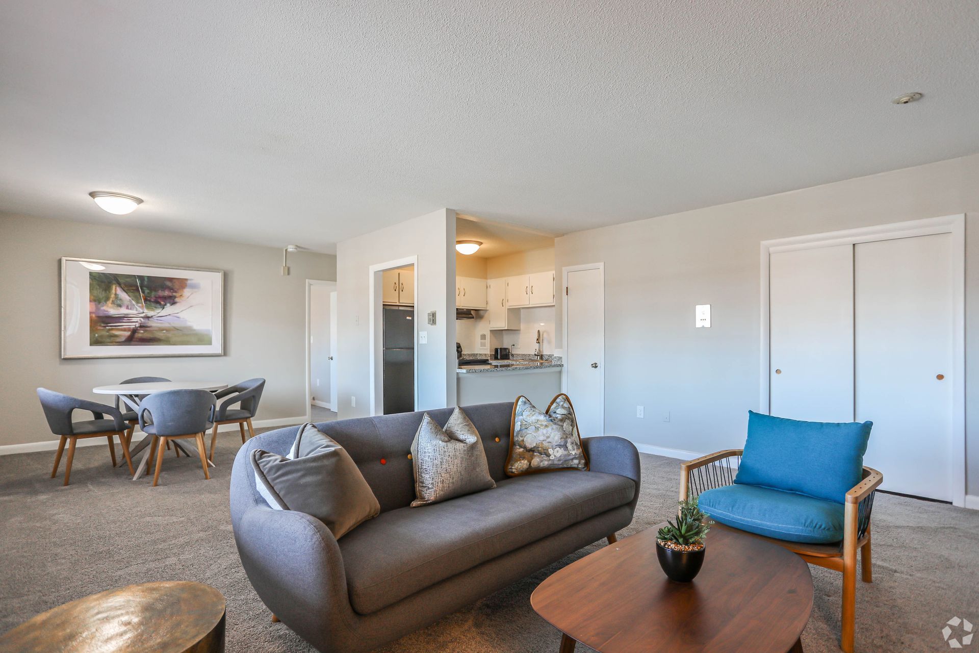 Living room with gray sofa, dining area, and open kitchen in neutral tones.