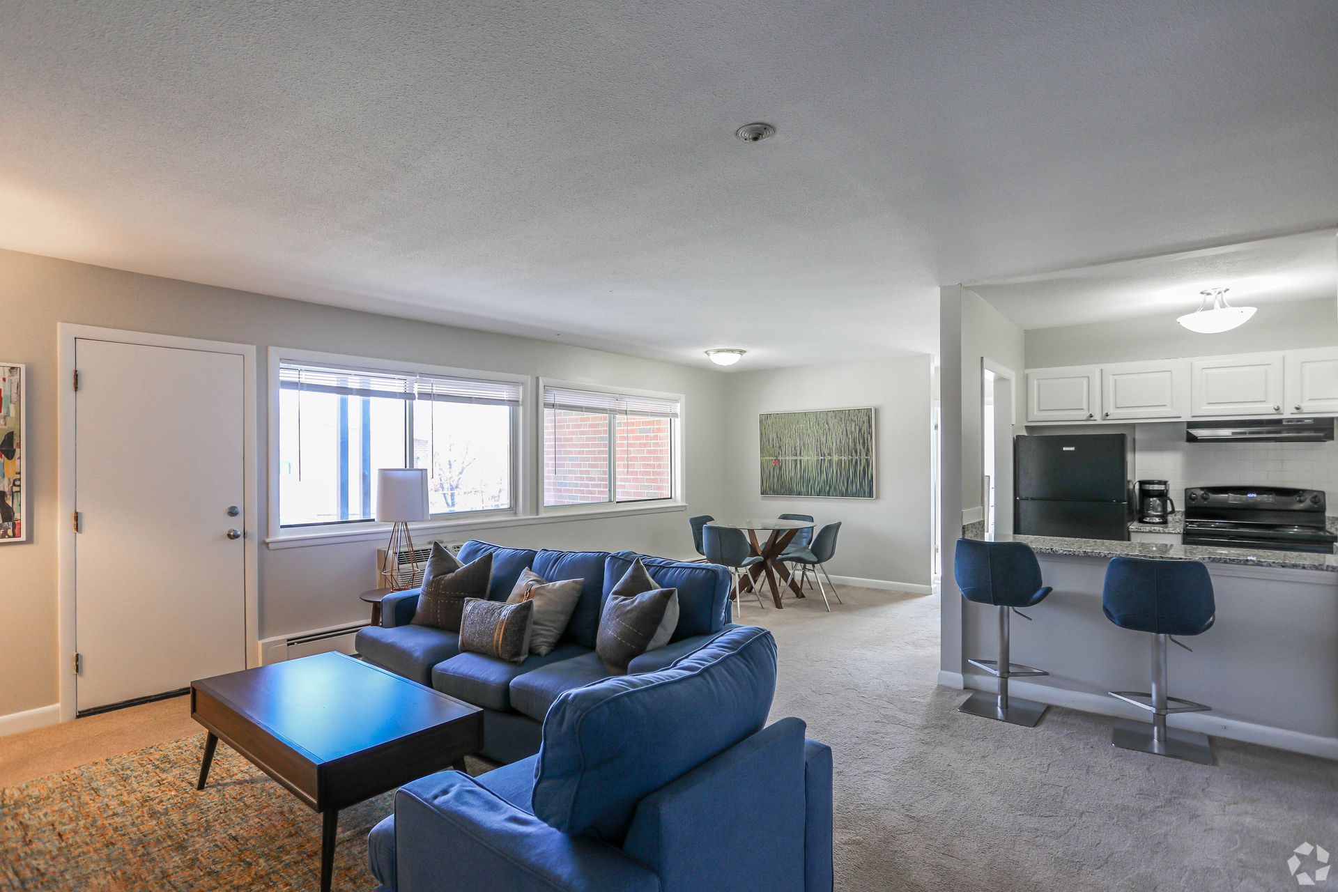 Living room with blue sofa and kitchen with bar stools.