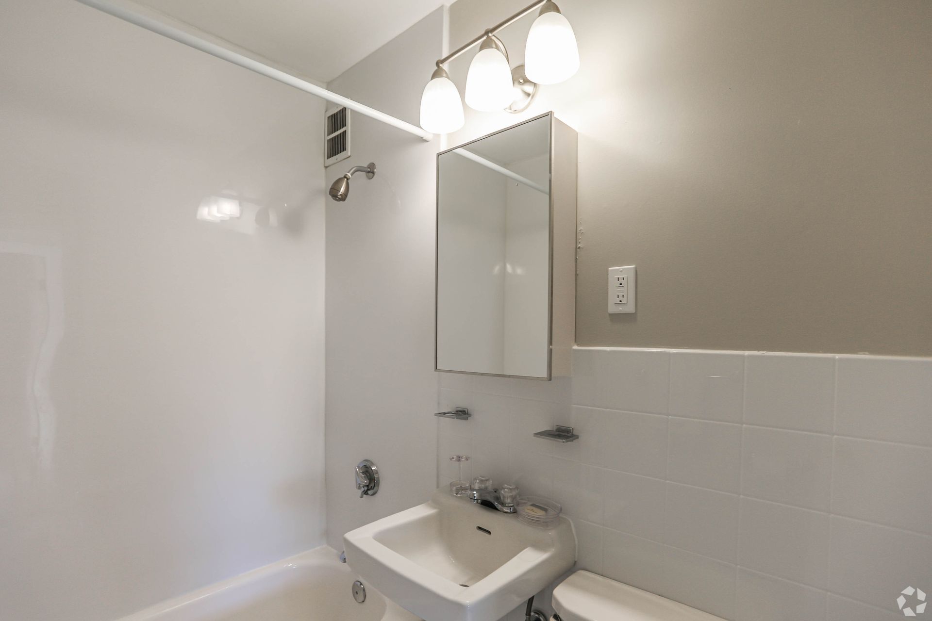 Bathroom with white fixtures, shower/tub combo, sink, mirror, and light fixture. Light gray walls.