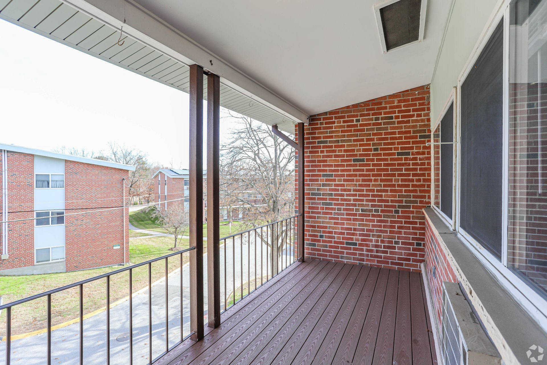 Balcony with wood flooring and metal railing, brick wall, and view of other buildings.