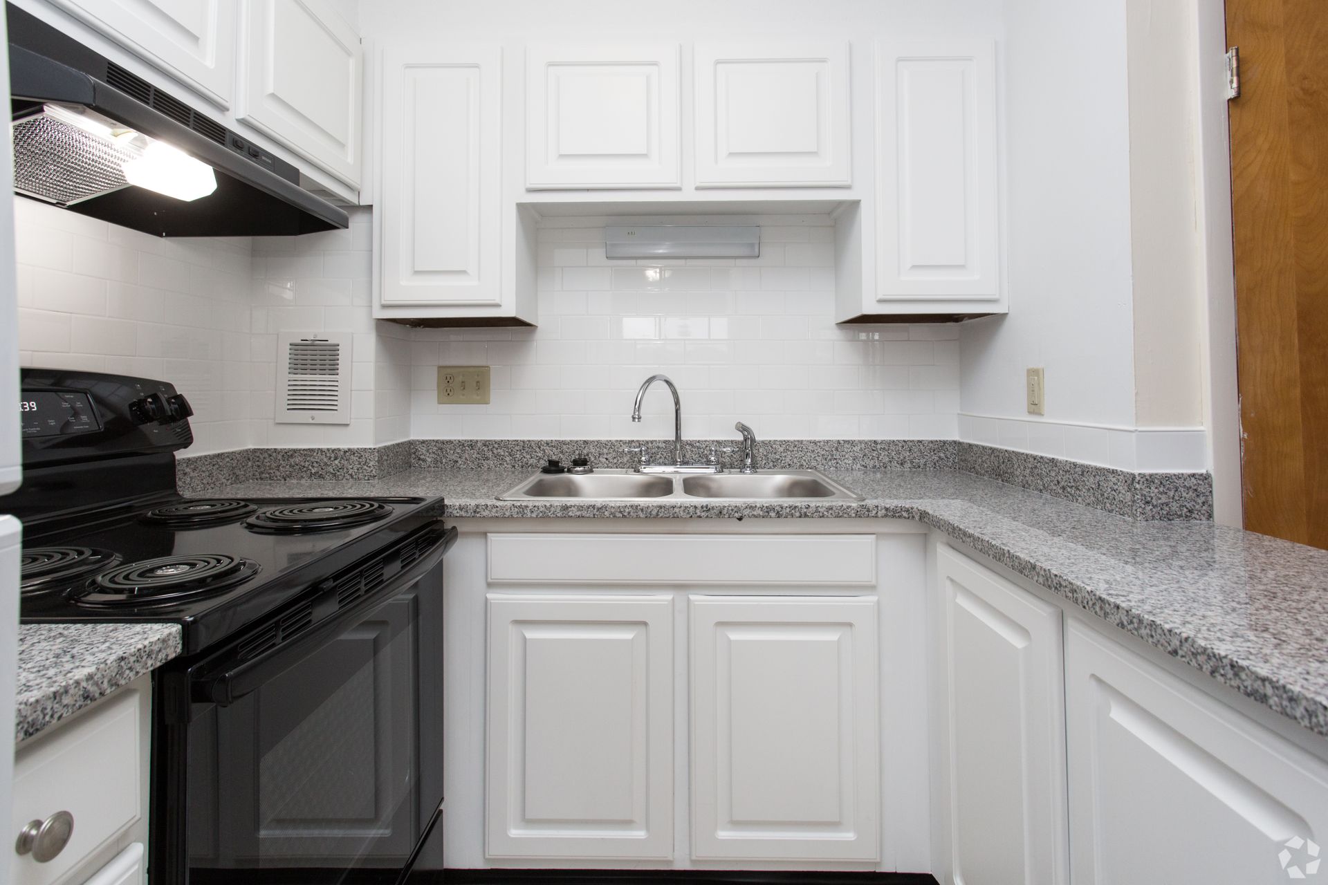 White kitchen cabinets with black appliances, gray countertops, and a double sink.